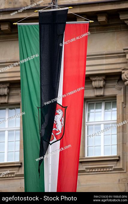 30 June 2021, North Rhine-Westphalia, Cologne: In memory of the victims of the Corona pandemic, a flag of mourning hangs on the state flag in front of the...
