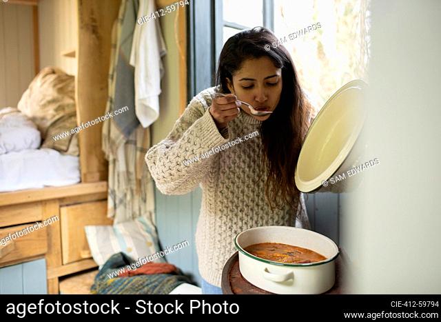Young woman cooking stew in tiny cabin