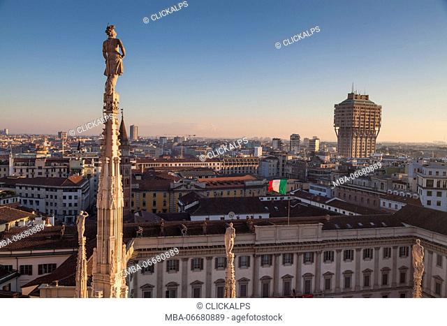 Milan, Lombardy, Italy. View of Velasca tower from the roof of Cathedral's Milan at sunset. In foreground there is a statue