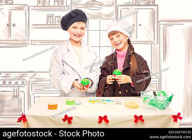 Beautiful boy and girl in chef clothes making christmas cupcakes. Children standing over kitchen drawing background