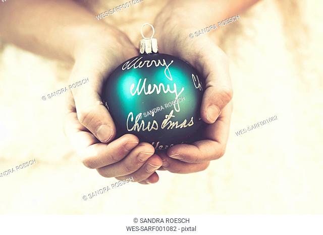 Girl's hands holding green Christmas bauble with the words 'Merry Christmas'