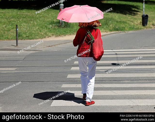 14 June 2022, North Rhine-Westphalia, Bonn: A woman walks through the city with an umbrella as a parasol. People in North Rhine-Westphalia can look forward to...