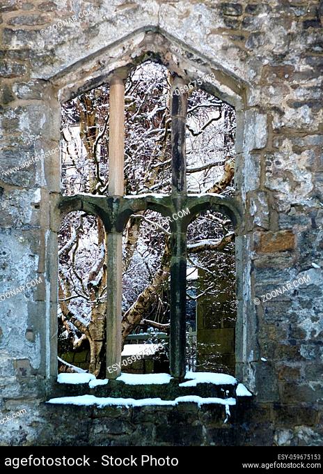 view through a window of a medieval ruined church in heptonstall yorkshire with snow covered trees behind the stone frame