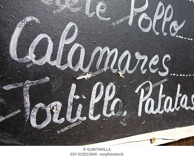 black placard spanish white handwritten in wall with typical menu food dishes in Spain restaurant like squid and potato omelette