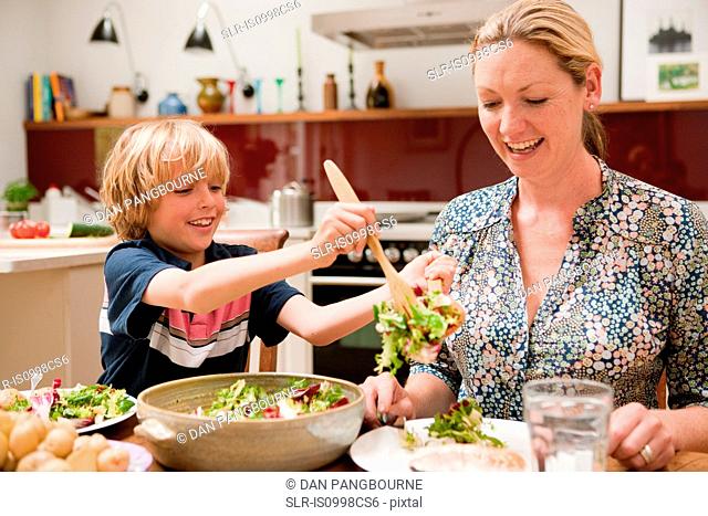 Son helping to serve salad for mother at the family dinner table