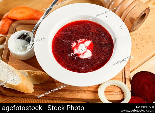 Ukrainian and Russian traditional beetroot soup - borscht in clay pot with sour cream, spice, garlic, pepper, dried herbs and bread on dark wooden background