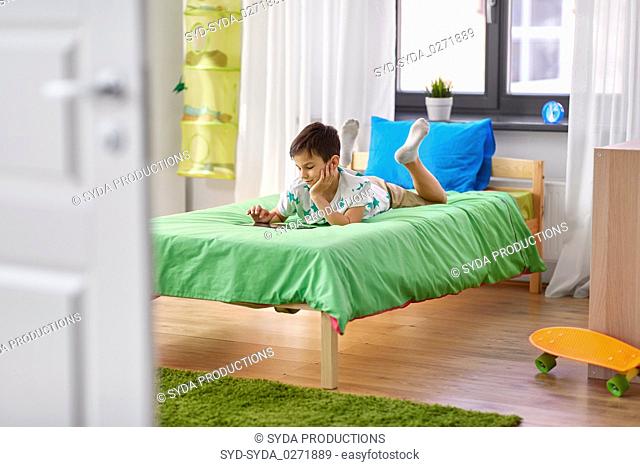 boy with tablet pc computer lying on bed at home