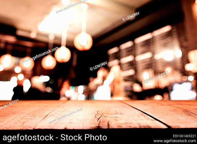 Empty blank wooden old deck table in front of abstract blurred festive background in bar, cafe, pub or restaurant with light spots and bokeh for product montage...