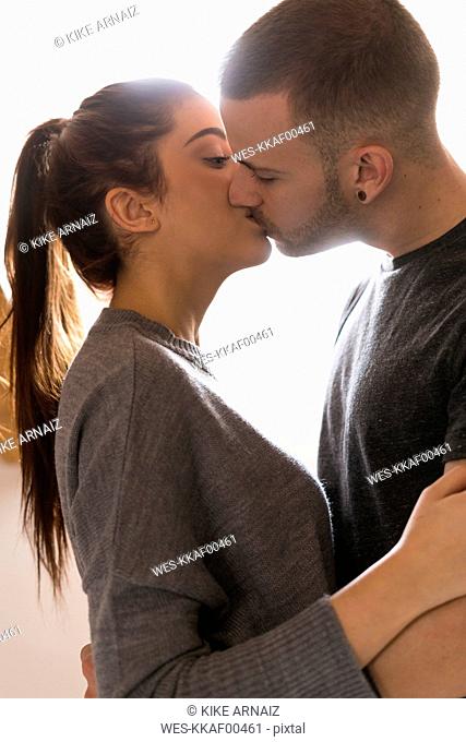 Amorous couple standing at home, kissing and ambracing passionately