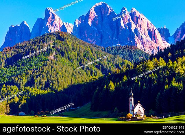 The gorgeous village Santa Maddalena in the Val di Funes Valley. Tyrol, Italy. Small white church with a bell among green lawns on the sunset