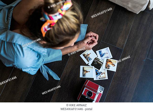 Young woman lying on the floor looking at instant photos of herself
