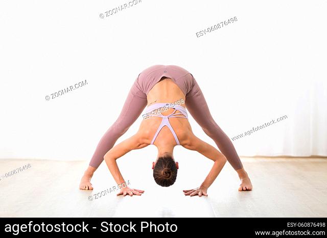 Portrait of gorgeous active sporty young woman practicing yoga in studio. Beautiful girl practice Dandayamana Bibhaktapada Paschimotthanasana