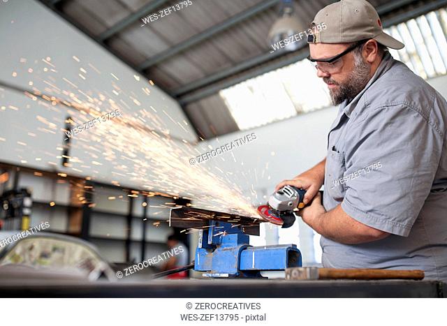 Mechanic using angle grinder in car workshop
