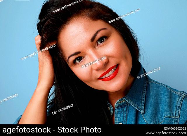 Portrait of smiling mature woman with red lips wearing denim shirt posing over blue background. High quality photo