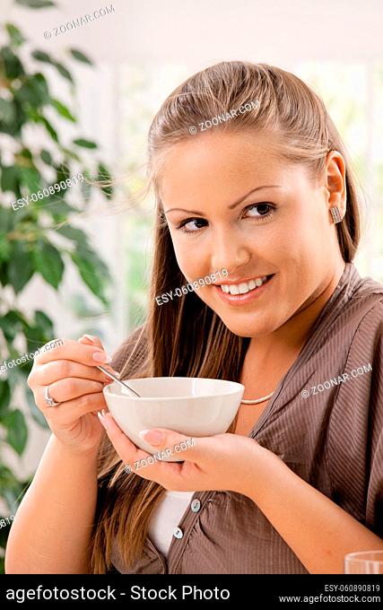 Happy young woman eating breakfast cereal, smiling