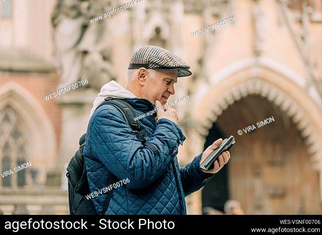 Senior man using smart phone standing in front of cathedral