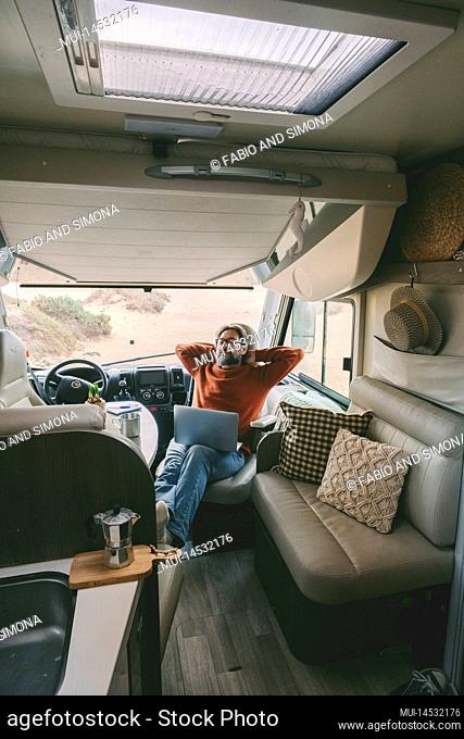 Adult man use laptop sitting inside a camper van. Concept of digital nomad lifestyle and wireless internet connection during travel