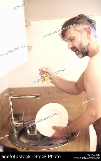 Nude man washing the dishes
