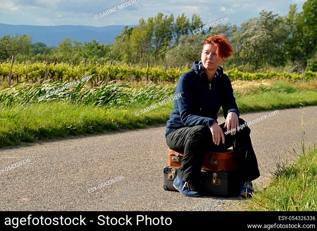selfconfident red-haired woman on vacation sitting on her suitcases on a road and waiting