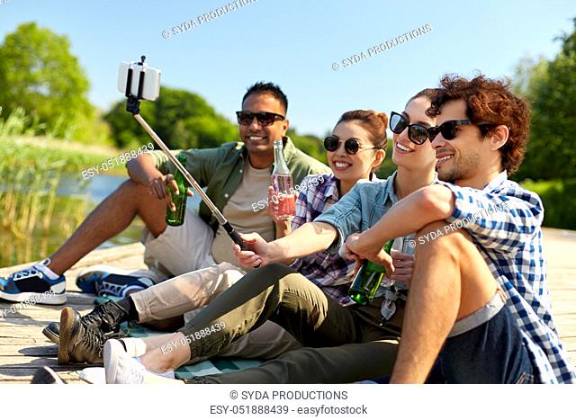 friends with drinks taking selfie on lake pier