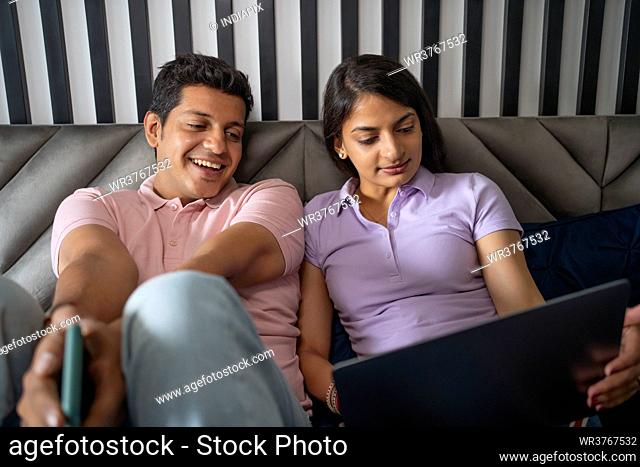 Young couple working on latop together lying in bed