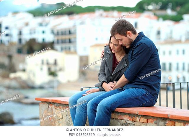 Sad woman and man comforting her on a ledge with a town in the background