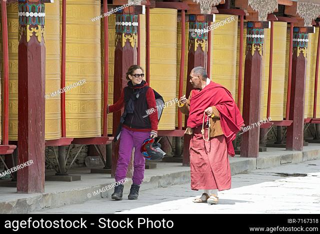 European young woman chatting with a Tibetan monk during the morning circumambulation, Tibetan: Kora of a Tibetan monastery in the grassland of Tagong