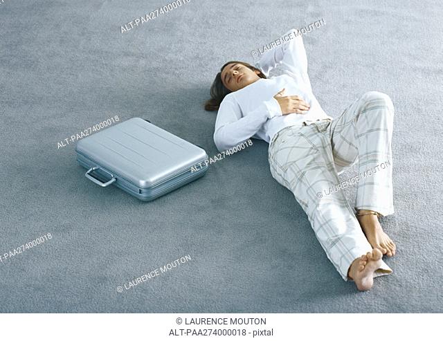 Man lying on carpet next to briefcase