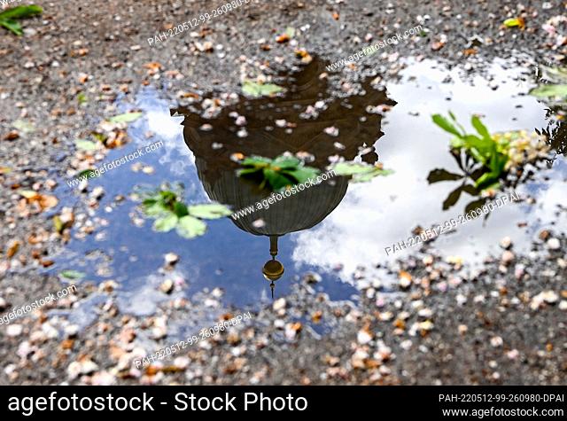 12 May 2022, Berlin: The tower of the cathedral and clouds reflected in a puddle in the Lustgarten. As usual in May, the so-called Ice Saints usually bring a...