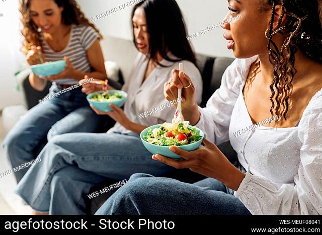 Woman eating salad with friends at home