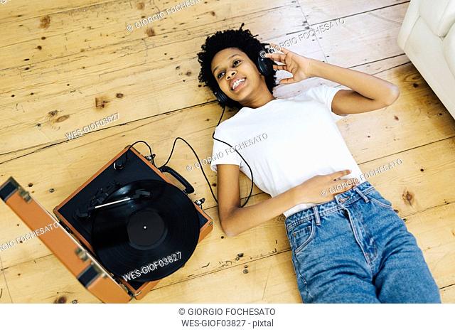 Young woman at home listening vinyl records, lying on ground
