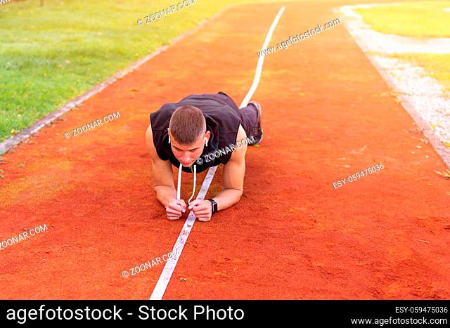 Young man doing plank exercise in the morning outdoor on the running race track