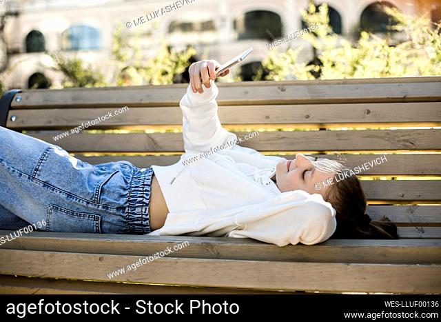 Girl taking selfie through smart phone while lying on bench