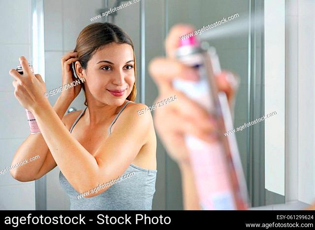 Young woman applying dry shampoo on her hair before going out. Fast and easy way to covering grey hair with instant spray dye