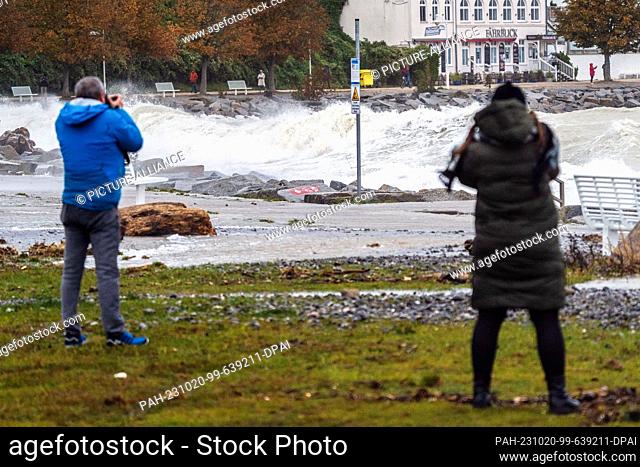20 October 2023, Mecklenburg-Western Pomerania, Sassnitz: People take pictures of the high waves on the beach promenade during a severe storm depression