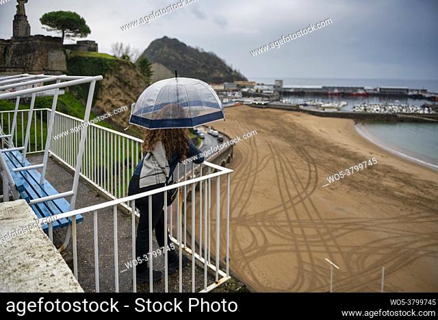 Woman with umbrella on a rainy day at a viewpoint overlooking the beach in Getaria, Basque Country, Spain