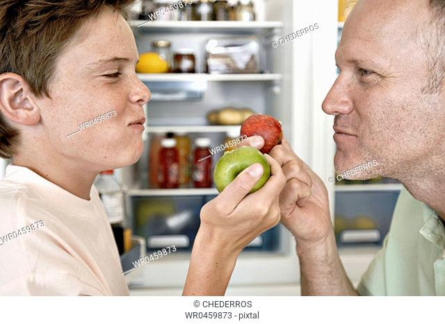 Side profile of a mature man and his son looking at each other and eating apples