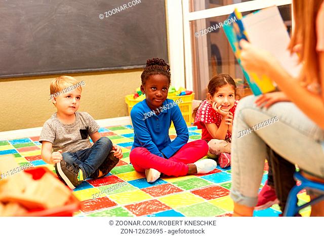 Gruppe Kinder hört aufmerksam zu beim Vorlesen aus einem spannenden Kinderbuch