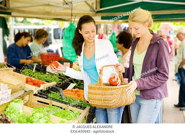 Two young women buying healthy fruits and vegetables on the market together