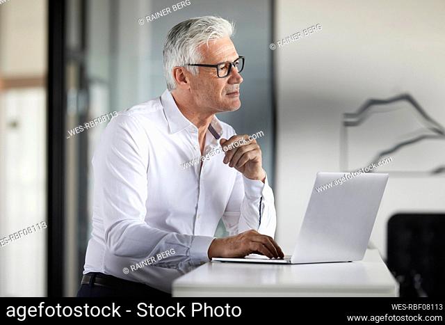 Businessman with laptop looking away in office