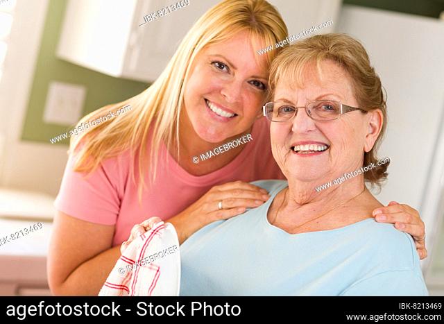 Portrait of smiling senior adult woman and young daughter at sink in kitchen