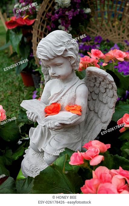 The little cupid was reading a book and surrounded by the beautiful flowers