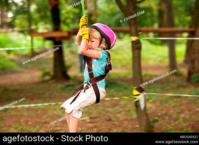 Girl in a helmet and safety equipment in adventure ropes park get down in the end of way