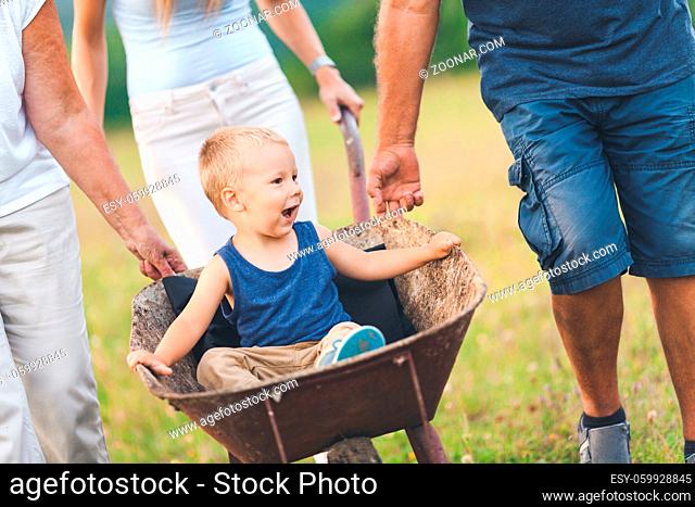 Family pushing their small child and grandchild in a wheelbarrow