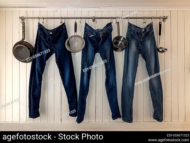Three pair of jeans hanging on a kitchen rail to dry in a small student apartment. Minimalistic, creative living, multipurpose. White wall background