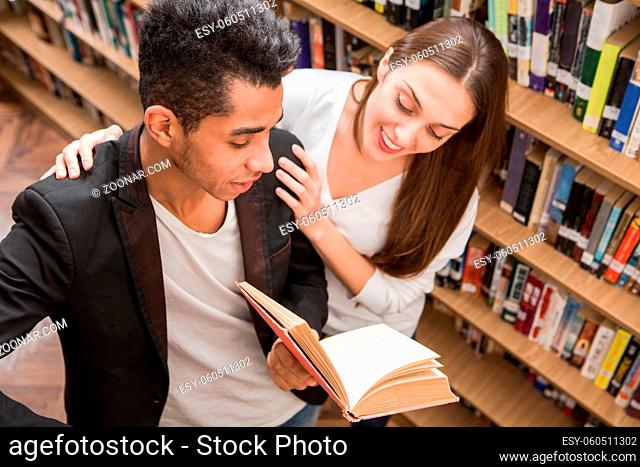Top view of students communicating in library. American man explaining to his girl-friend something important in science