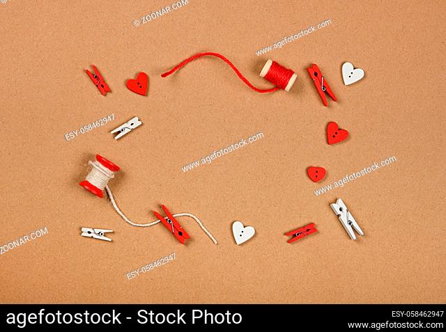 Frame of Valentine gift decorations, twine, clothespins and hearts over brown paper background, close up flat lay, elevated top view, directly above