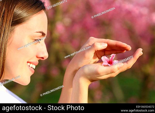 Profile of a happy woman protecting flower in her hands in a field