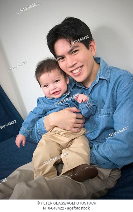 Asian man sitting on a bed with his Eurasian toddler son