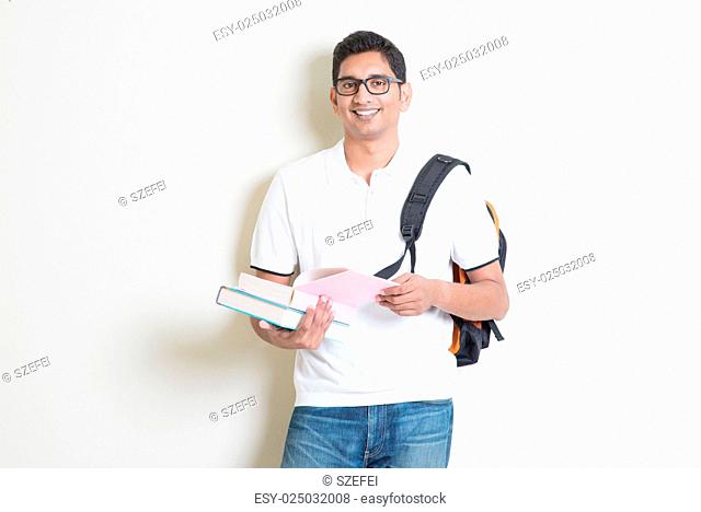 Portrait of adult Indian college student with bag and books. Asian man standing on plain background with shadow and copy space